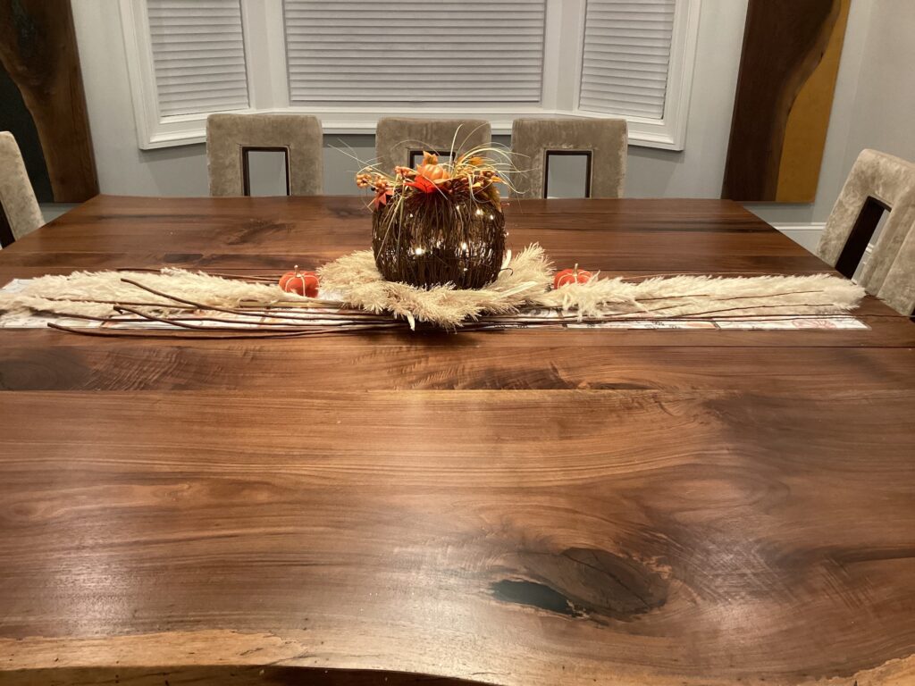 A wooden pumpkin with orange and red flowers and a beige neutral table runner as a thanksgiving tablescape kit