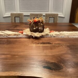 A wooden pumpkin with orange and red flowers and a beige neutral table runner as a thanksgiving tablescape kit